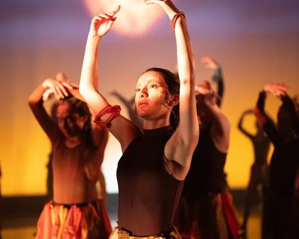 Dancer leading an ensemble beneath warm stage lighting